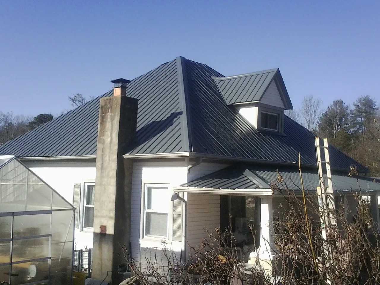 Dark blue standing seam metal roof on a white farmhouse with dormer — Slate & Tile Roof Repair by Roofing Brothers in White Rock