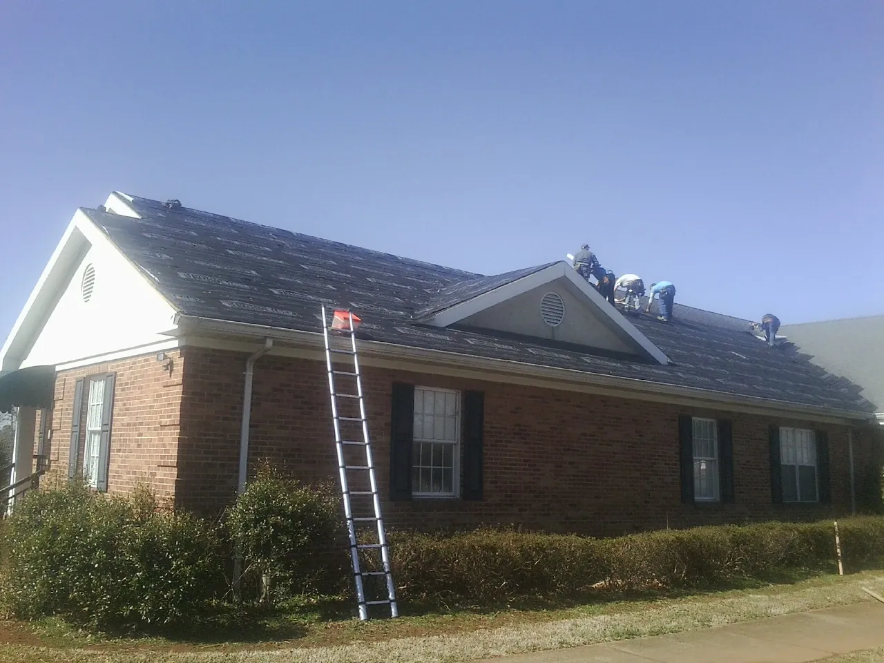 Crew tearing shingles off a brick ranch roof with a ladder set — Metal Roof Repair work by our crew in White Rock
