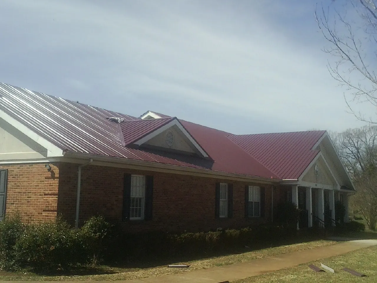 Red metal roof with gabled entries on a long brick building, from a Hail Damage Roof Repair job in White Rock