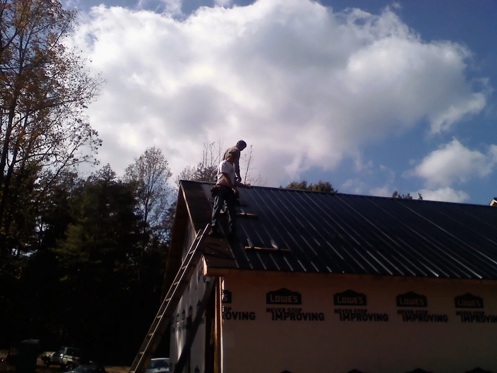 Roofer fastening dark metal panels high against a cloudy sky, from a Roof Inspection job in White Rock
