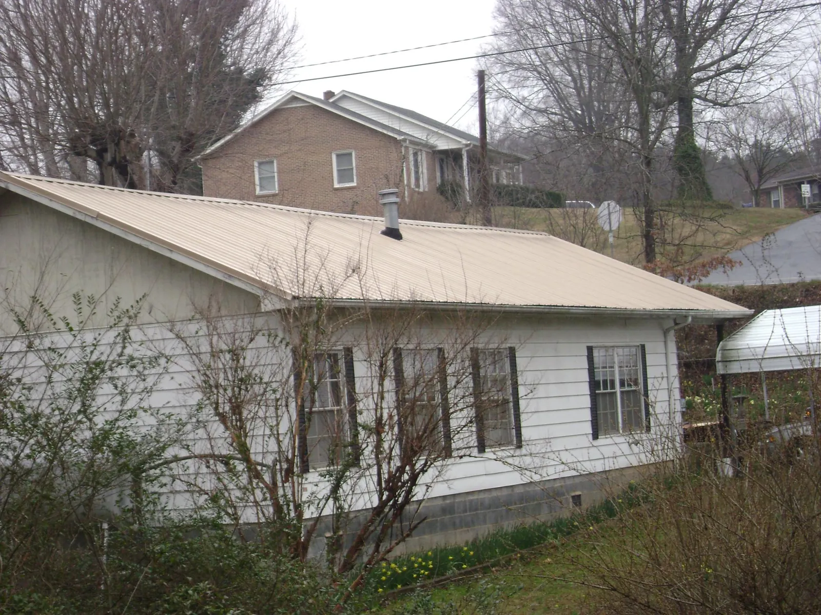 Tan metal roof on a white sided house set into a hillside — Commercial Roofing by Roofing Brothers in White Rock